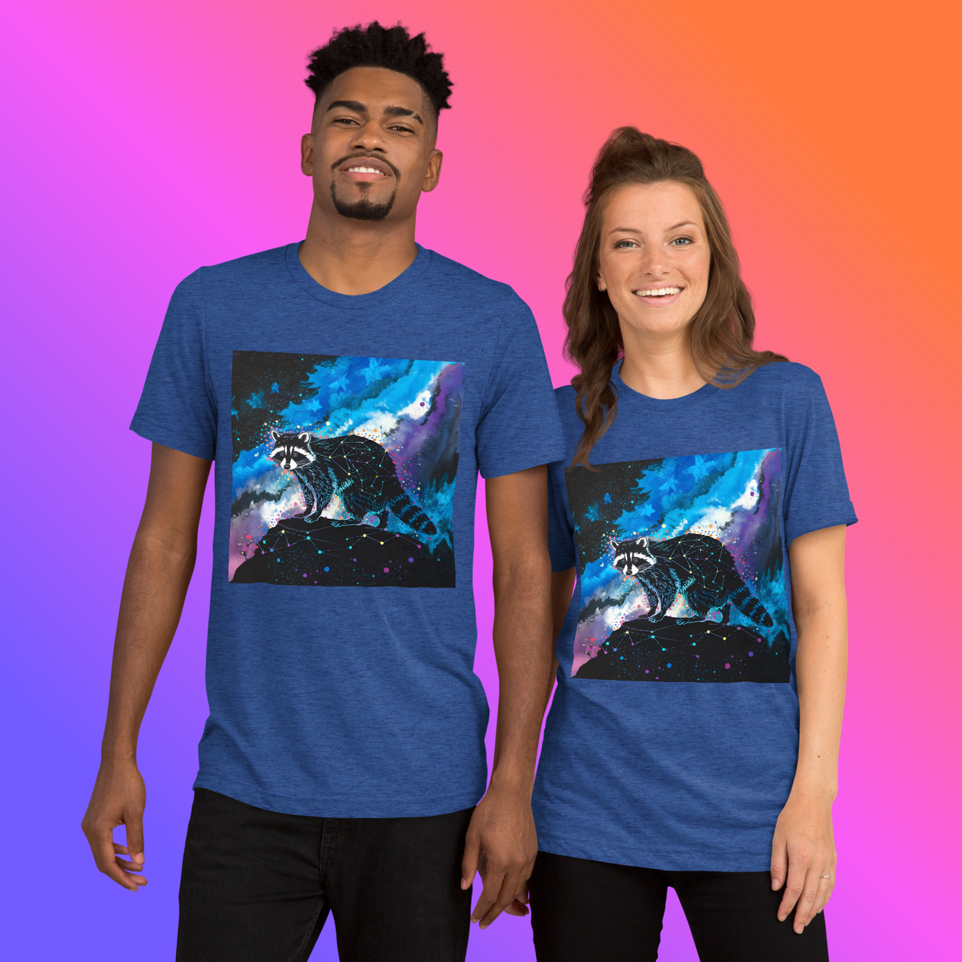 Cosmic Bandit Unisex T-Shirt hero lifestyle shot — smiling Black male model and smiling White female model both wearing true royal triblend tee showing front graphic of geometric constellation raccoon perched on dark rock against swirling blue purple and teal cosmic nebula with neon star splatter against pink to orange gradient background
