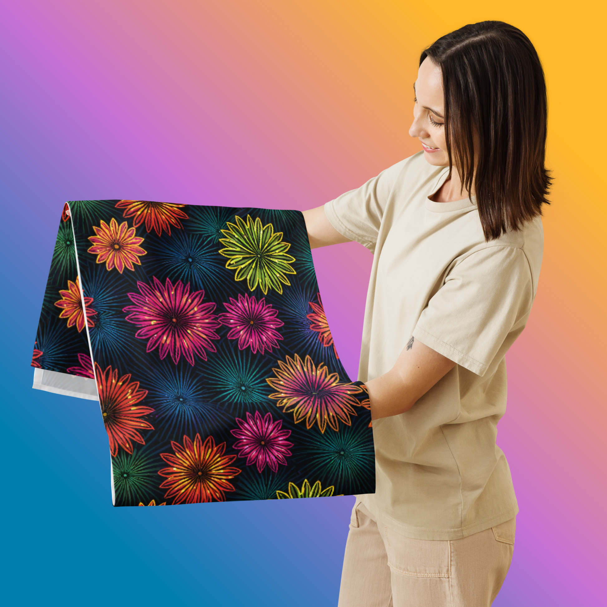 Fluorescent Floral Table Runner hero lifestyle shot — smiling White female model in cream oversized tee holding folded table runner showing all-over print of neon pink orange yellow-green and teal daisy-like flowers with radiating petal details on dark navy background against blue to orange gradient background