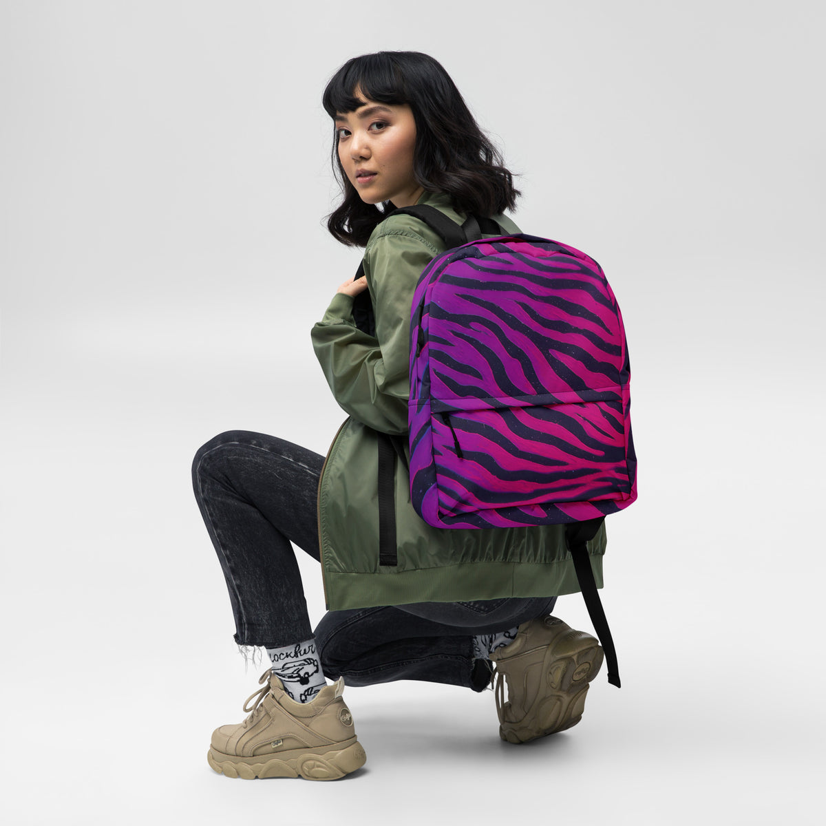 Neon Tiger Stripe backpack lifestyle shot — female model crouching wearing backpack in studio setting