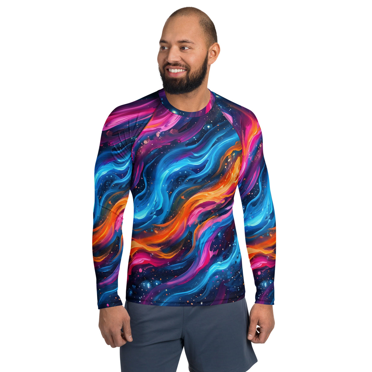 Male model smiling and wearing the Cosmic Surge all-over print men's rash guard featuring swirling neon galaxy waves in blue, pink, and orange, paired with grey shorts
