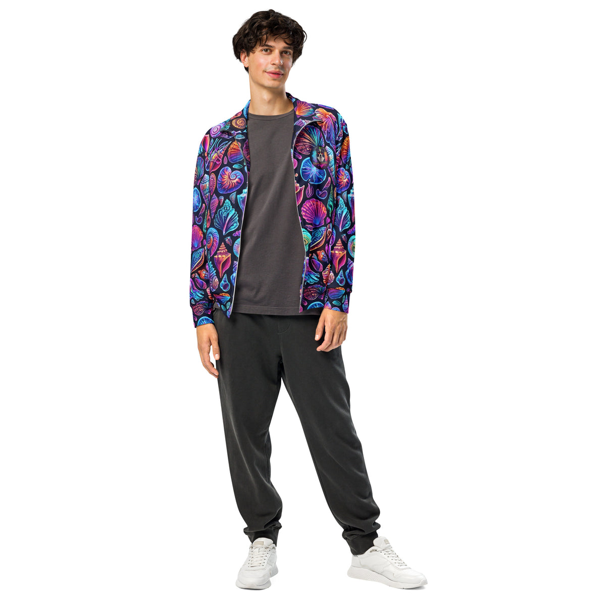 Male model wearing the Chromashell Unisex Track Jacket zipped up, front view showing the bold neon seashell all-over print with scallops, nautilus spirals, and conch shells in electric purple, pink, teal, and orange on black