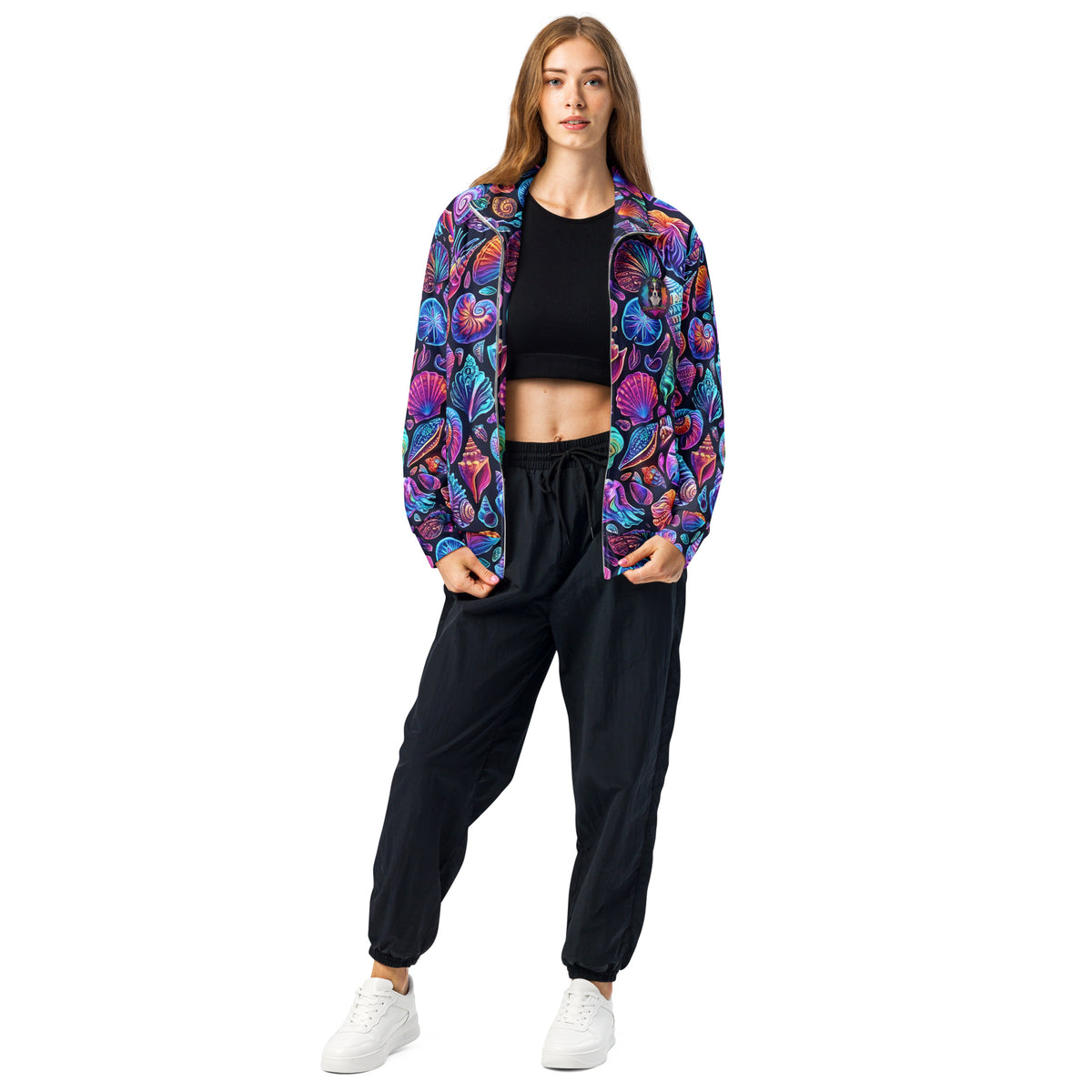 Female model wearing the Chromashell Track Jacket open over a black crop top and joggers, front view showing the bold neon seashell print with scallops, nautilus, and conch shells