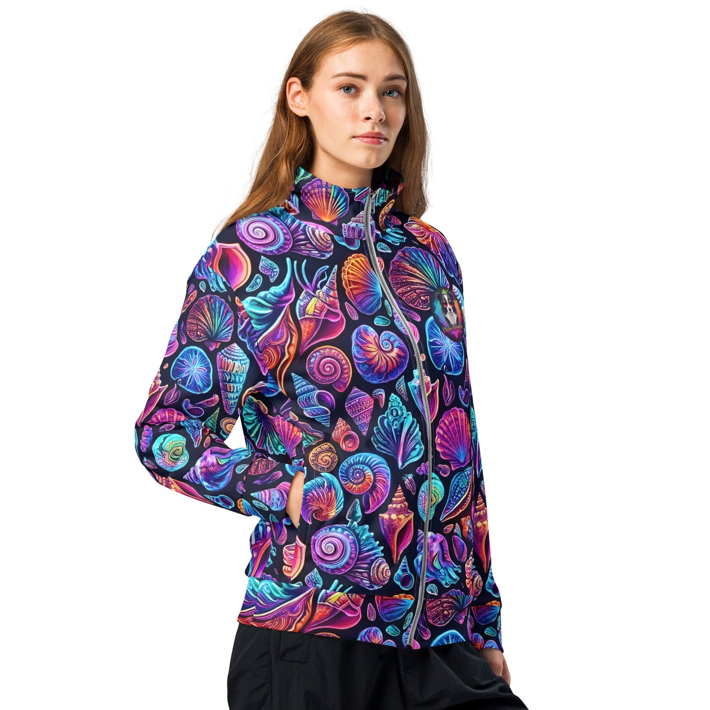 Three-quarter view of female model wearing the Chromashell neon seashell track jacket zipped up, showing the wrap-around print with spiral shells and scallops glowing in purple and teal
