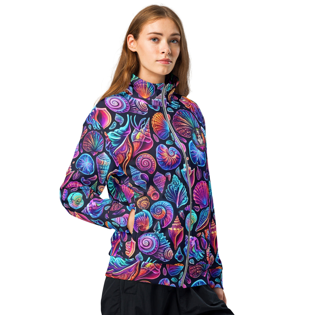 Three-quarter view of female model wearing the Chromashell neon seashell track jacket zipped up, showing the wrap-around print with spiral shells and scallops glowing in purple and teal