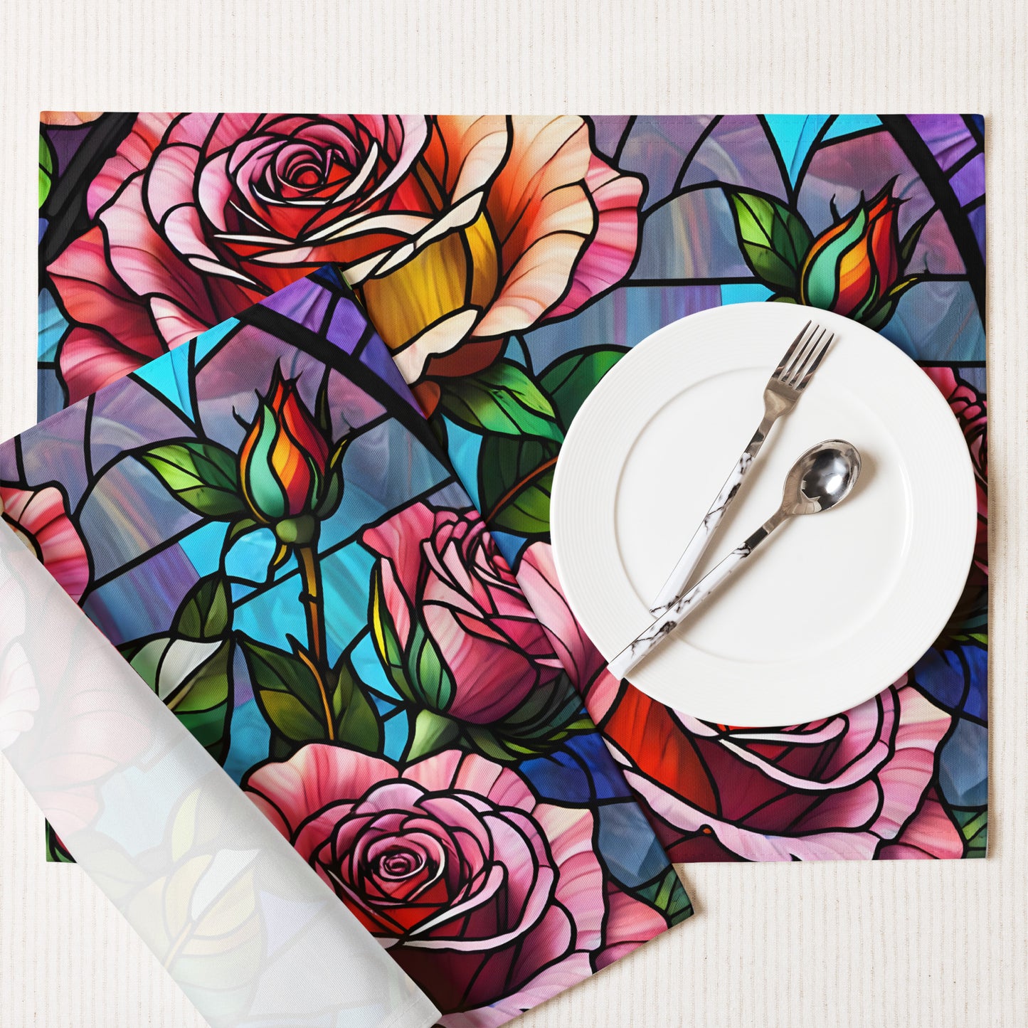 Stained Roses Placemat Set lifestyle shot — single placemat set on white linen surface with white plate fork and spoon showing stained glass mosaic design of large pink and red roses with green leaves and colorful geometric background panels in blue purple and teal