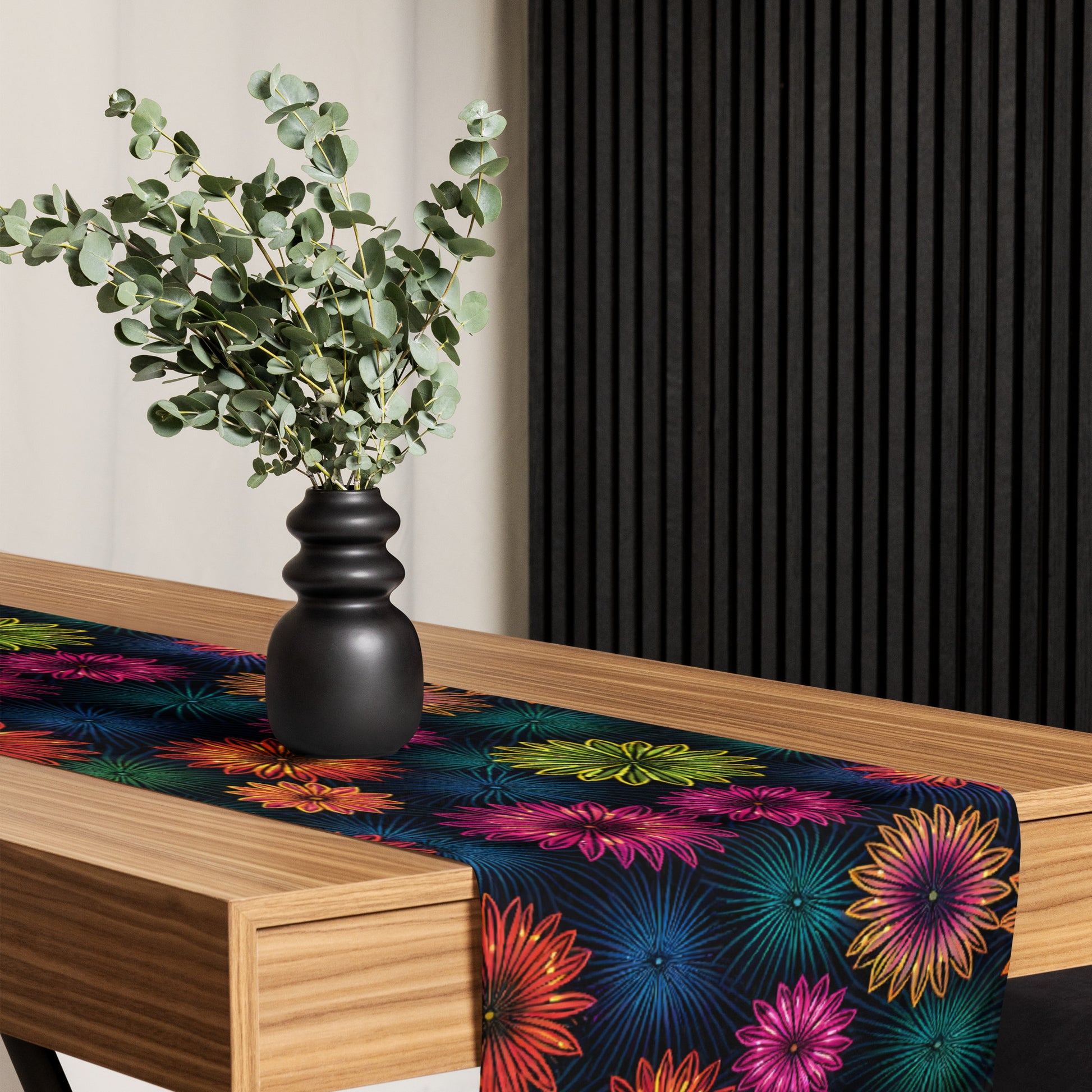 Fluorescent Floral Table Runner hero product shot — table runner draped across dark wood dining table showing full all-over print of neon pink orange yellow-green and teal daisy-like flowers with radiating petal details on dark navy background against pink to purple gradient background